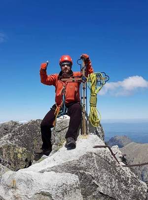 Na zdjęciu alpinista z rękami w górze na szczycie.