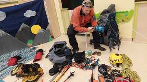 Zdjęcie przedstawia mężczyznę w przedszkolu, który pokazuje rozłożony sprzęt alpinistyczny.