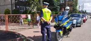 policjant stojący przed wejściem do szkoły, motocykl policyjny, dzieci wychodzące ze szkoły