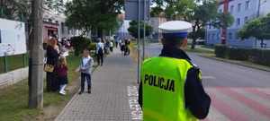 policjant stojący przy szkole, dzieci z rodzicami idący do szkoły