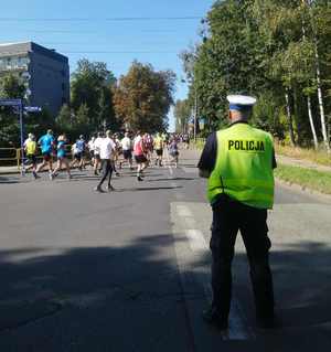 Zdjęcie przedstawia policjanta ruchu drogowego, który patrzy w stronę biegaczy.