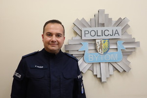 Na zdjęciu policjant posterunkowy Przemysław Mazur w tle odznaka policyjna z napisem Policja Bytom.