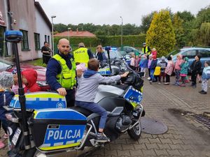 Na zdjęciu widzimy policjantów ruchu drogowego, którzy pokazują dzieciom na festynie motocykle policyjne.