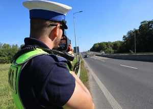 Zdjęcie przedstawia policjanta, który dokonuje pomiaru prędkości.