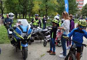 Zdjęcie przedstawia motocykle policyjne, które oglądają uczestnicy wyścigów rowerowych oraz widzimy policjanta ruchu drogowego.