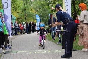 Na zdjęciu widzimy policjantkę, która klaszcze i linię startu oraz dziewczynkę jadącą na rowerze.