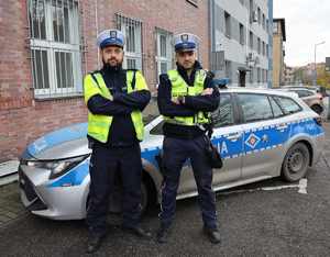 Zdjęcie przedstawia dwóch policjantów ruchu drogowego, którzy stoją przed radiowozem.