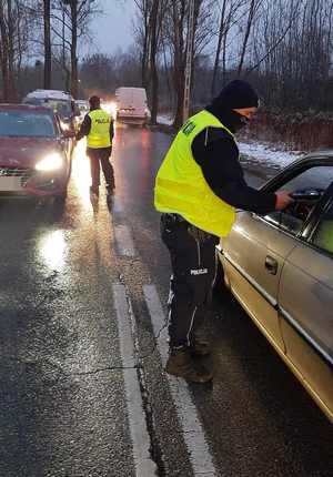 Na zdjęciu policjanci na jezdni kontrolują stan trzeźwości kierujących pojazdami.