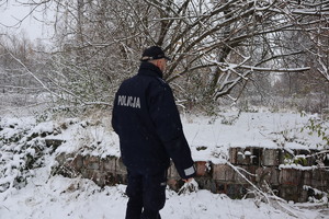 Zdjęcie przedstawia policjanta przy ruinach pustostanu.