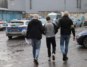 Policjanci prowadzą zatrzymanego mężczyznę przez plac wewnętrzny Komendy Miejskiej Policji w Bytomiu, widoczne zaparkowane radiowozy.