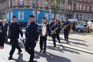 Na zdjęciu maszerujący policjanci trzymający w dłoniach instrumenty.