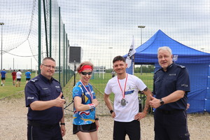 Na zdjęciu cztery osoby z uniesionymi kciukami do góry. Medalista i medalistka pośrodku, po bokach dwóch oficerów policji.