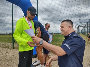 Na zdjęciu policjant wręczający dyplom mężczyźnie na podium