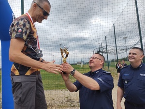 Na zdjęciu dwóch oficerów wręczających puchar mężczyźnie na podium