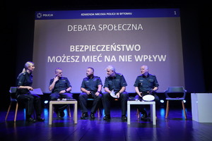 Na zdjęciu pięć osób siedzących na krzesłach, na scenie. Czterech policjantów i jedna policjantka. Za nimi wyświetlony napis Debata społeczna, Bezpieczeństwo, możesz mieć na nie wpływ.