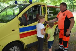 Na zdjęciu dzieci przed ambulansem, obok ratownik medyczny