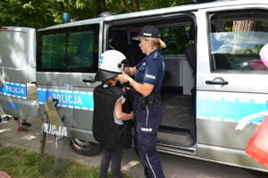 Na zdjęciu policjantka, która zakłada dziecku kask, ma na sobie sprzęt służbowy czarną kamizelkę.