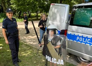 Na zdjęciu radiowóz policyjny, obok policjantka i osoby