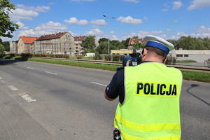 Na zdjęciu policjant w żółtej kamizelce wykonuje pomiar prędkości