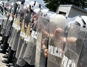 Na zdjęciu policjanci ubrani w czarne kamizelki taktyczne, białe kaski, trzymają w dłoniach tarcze z napisem Policja.