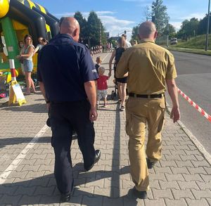 Na zdjęciu dwóch mundurowych idących chodnikiem, widok z tyłu. Jeden w granatowym a drugi w kremowym mundurze.