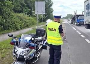 Na zdjęciu policjant wykonujący pomiar prędkości, obok motocykl służbowy.