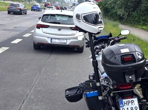 Na zdjęciu pojazd osobowy srebrnego koloru, obok motocykl służbowy, na motocyklu widoczny biały kask.