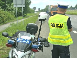 Na zdjęciu policjant wykonujący pomiar prędkości, obok motocykl służbowy.