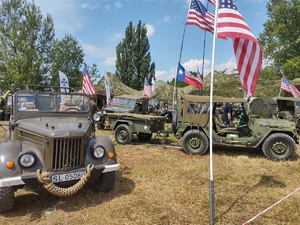 Na zdjęciu pojazdy militarne, dookoła nich flagi.