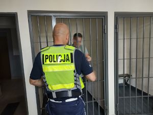 Na zdjęciu widzimy policjanta stojącego przy klacie, za którą znajduje się zatrzymany mężczyzna