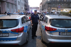 Na zdjęciu policjant stojący pomiędzy dwoma radiowozami