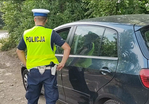 Na zdjęciu policjant stojący przy samochodzie.
