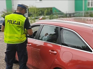 Na zdjęciu policjant stojący przy samochodzie czerwonego koloru.
