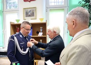 Na zdjęciu komendant w mundurze, obok dwaj mężczyźni, jeden z nich przypina policjantowi medal.