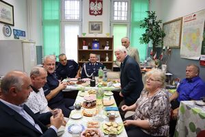 Na zdjęciu siedzące przy nakrytym stole osoby, w tym mundurowi, pośrodku komendant.