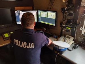 Na zdjęciu policjant siedzący przed dwoma  monitorami, na których widzimy poruszające się pojazdy na drodze.