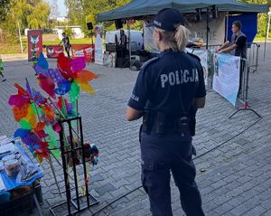 Na zdjęciu umundurowana policjanta, przed nią stoisko, obok niej kolorowe wietraki.