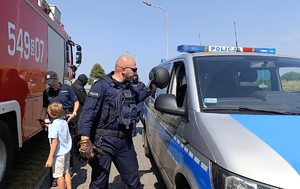 Na zdjęciu widoczni policjanci i kilkuletni chłopiec, obok radiowóz policyjny i fragment wozu strażackiego.