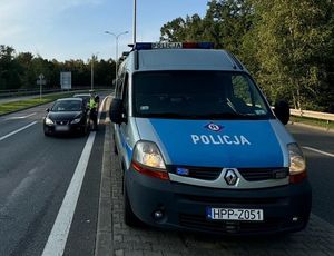 Na zdjęciu radiowóz, obok policjant na drodze sprawdzający stan trzeźwości kierujących.