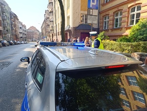 Na zdjęciu radiowóz policyjny i  policjant bytomskiej drogówki przed budynkiem szkoły, obok przemieszczjące się osoby.