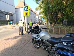 Na zdjęciu motocykl policyjny i policjanci bytomskiej drogówki stojący przy przejściu dla pieszych.