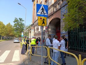 Na zdjęciu policjanci bytomskiej drogówki wraz ze strażniczką miejską, przed budynkiem szkoły, dookoła nich przemieszczjące się osoby.