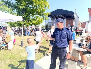 Na zdjęciu Pierwszy Zastępca Komendanta Miejskiego Policji w Bytomiu przybija piątkę z kilkuletnim chłopcem, dookoła uczestnicy wydarzenia, za nimi scena.