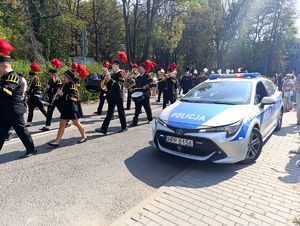 Na zdjęciu maszerujące osoby, obok nich radiowóz policyjny.