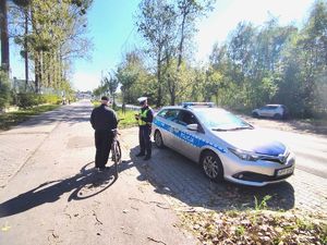 Na zdjęciu mężczyzna przy rowerze, obok policjant i radiowóz policyjny.