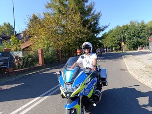 Na zdjęciu policjant na motocyklu służbowym, za nim biegnące w półmaratonie osoby.