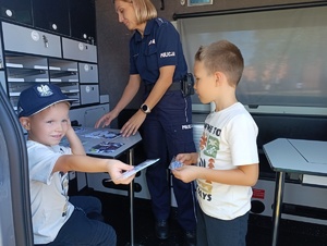 Na zdjęciu w radiowozie policyjnym widzimy dwóch chłopów a przy nich policjantkę.