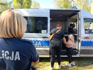 Na zdjęciu policjantka oraz kobieta z dzieckiem wchodząca do policyjnego pojazdu.