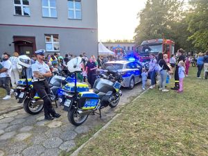 Na zdjęciu radiowóz policyjny, wóz strażacki, dwa motocykle policyjne, policjanci i uczestnicy wydarzenia.