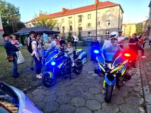 Na zdjęciu zgromadzone osoby, pośrodku dwa motocykle policyjne na których znajdują się dzieci, obok policjant i policjantka.